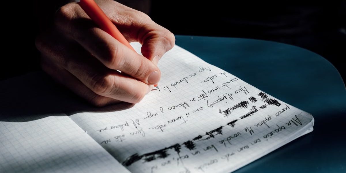 A person's hand writing in a notebook on a sunny day, showing detailed cursive notes.
