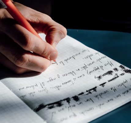 A person's hand writing in a notebook on a sunny day, showing detailed cursive notes.